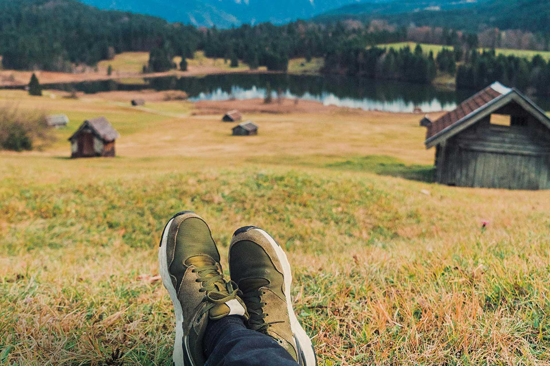 Feet in olive green shoes against the background of a meadow with wooden barns.