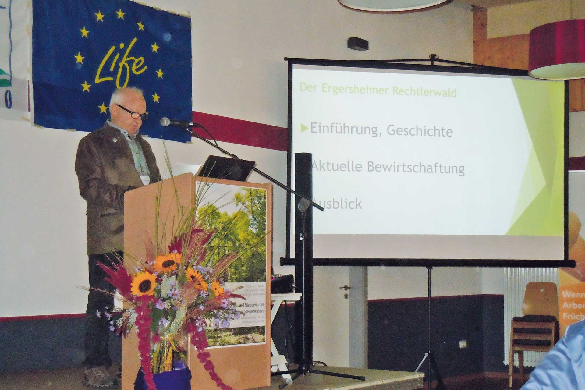 Speech at the event of the administrative districts of Lower and Middle Franconia: An elderly man stands at a flower-decorated podium in front of a microphone.