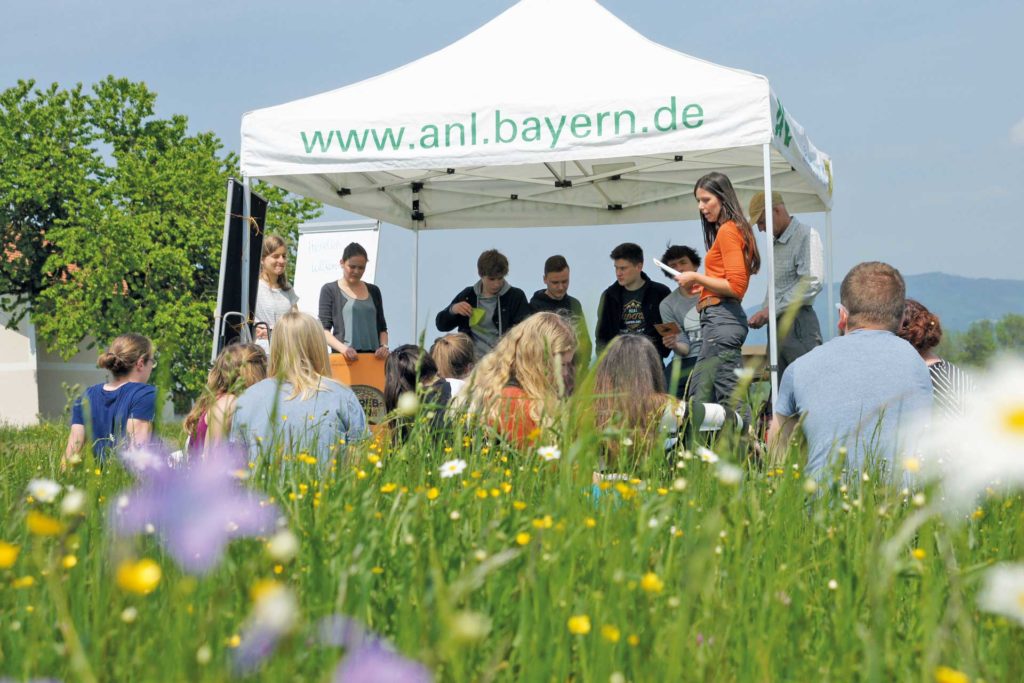 Jugendliche sammeln sich bei Sonnenschein unter dem www.anl.bayern.de Zelt.