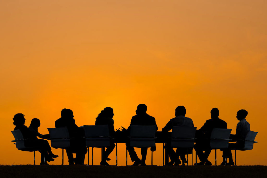 People sitting at a table talking in front of an orange background.