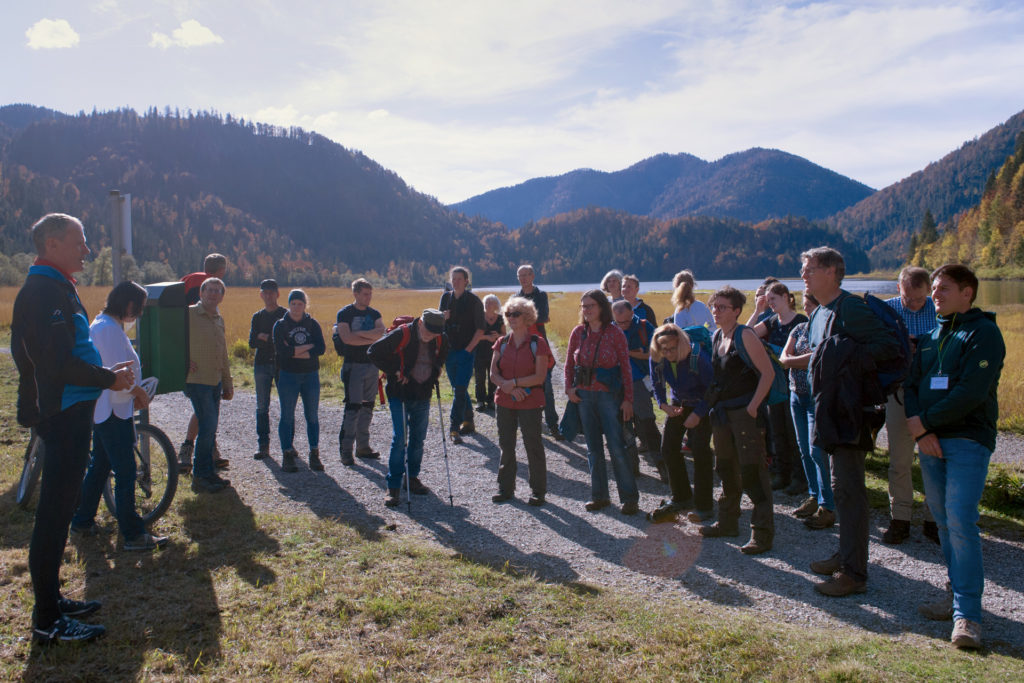 Exkursionsgruppe mit circa 25 Teilnehmern, im Hintergrund der Weitsee und Berge.