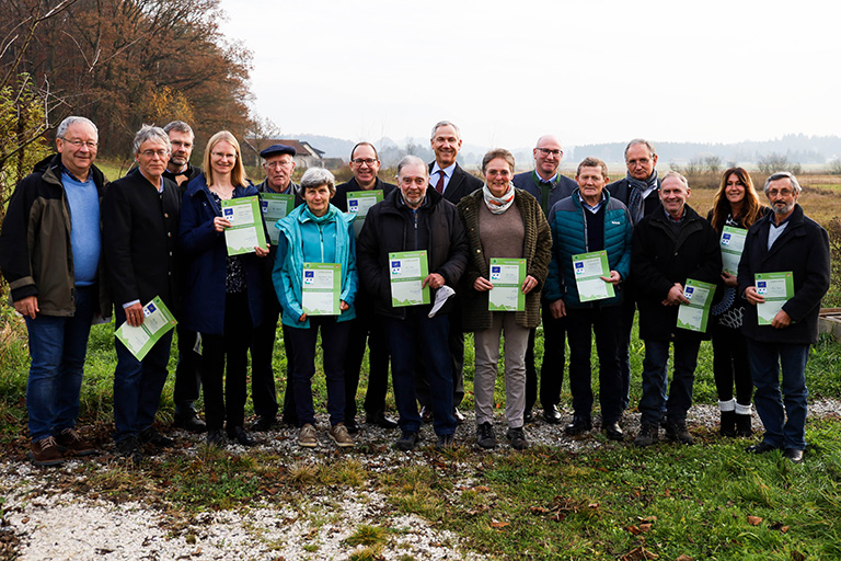 Eine Gruppe von Personen in Winterkleidung steht auf einer Wiese. Alle halten Urkunden in den Händen.