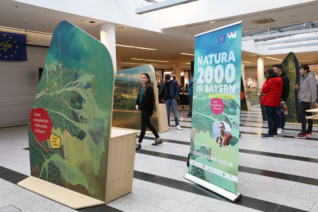 Zwischen den Stelen der Wanderausstellung gehen mehrere Menschen umher