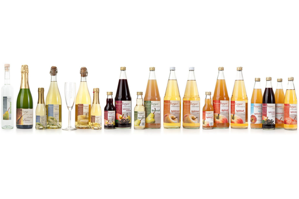 Säfte und alkoholische Getränke in Glasflaschen stehen in einer Reihe vor weißem Hintergrund.