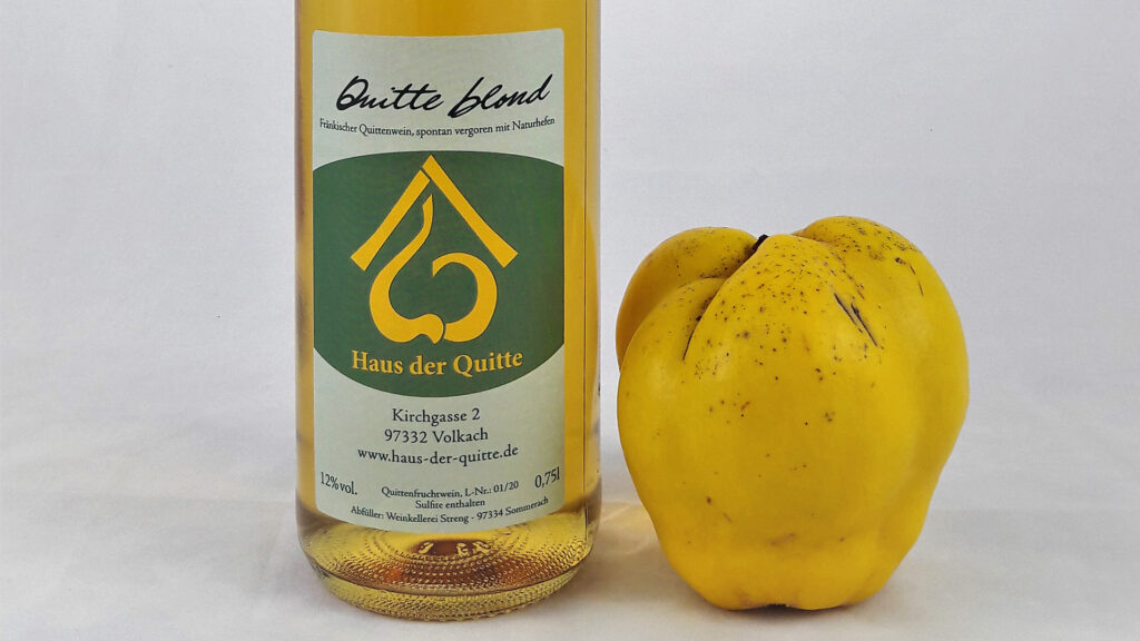 Eine Flasche Quittenwein blond, daneben eine reife, gelbe Quitte