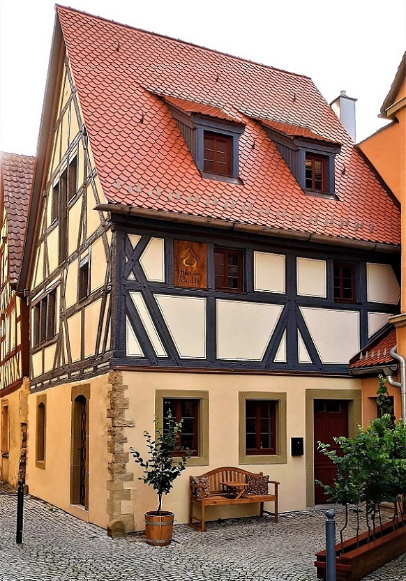 Ein altes Fachwerkhaus mit rotem Ziegeldach in einer mit Kopfsteinen gepflasterten Gasse.