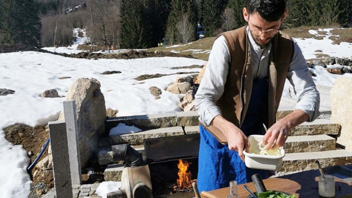 Max Müller kocht in einer improvisierten Outdoor-Küche. Im Hintergrund sieht man die Berge.