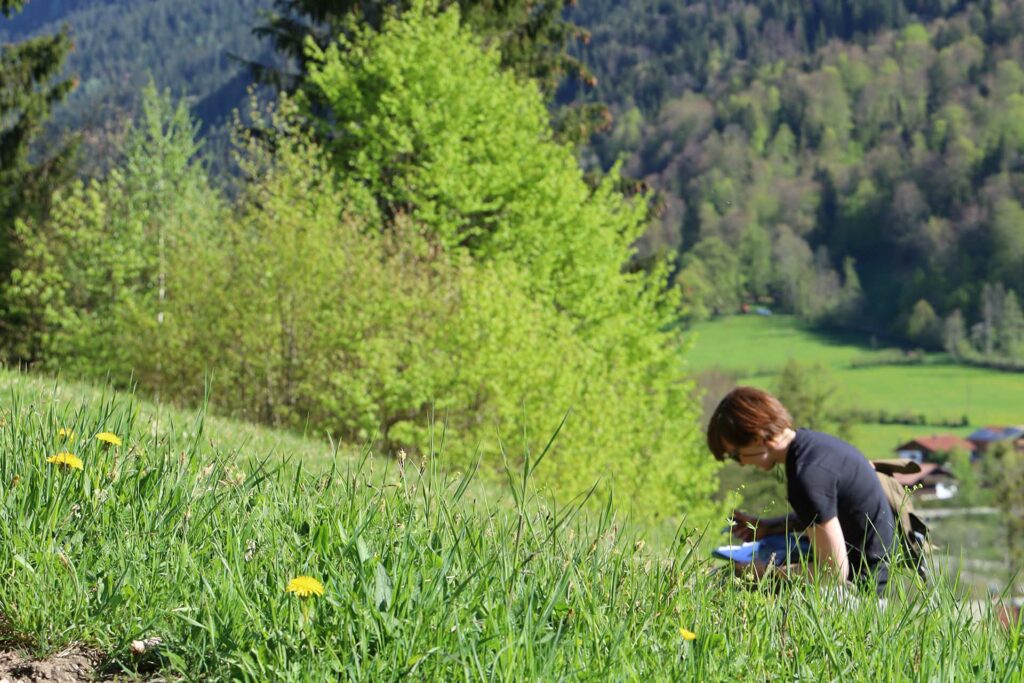 Auf einer frühlingsgrünen Wiese such eine rothaarige FRau nach Schlüsselblumen.