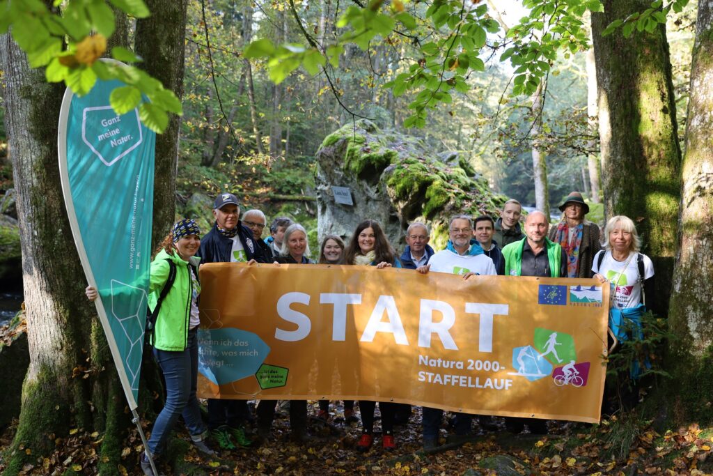 A group of people on a forest trail holding a banner that reads START