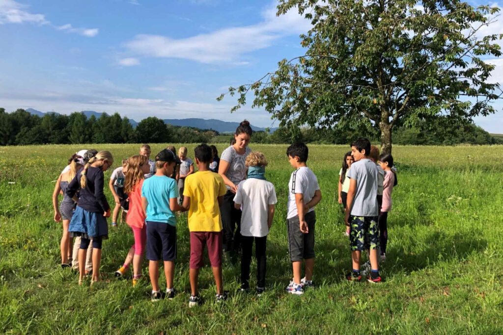 Eine Gruppe von Kindern steht in einem Kreis auf einer grünen Wiese.