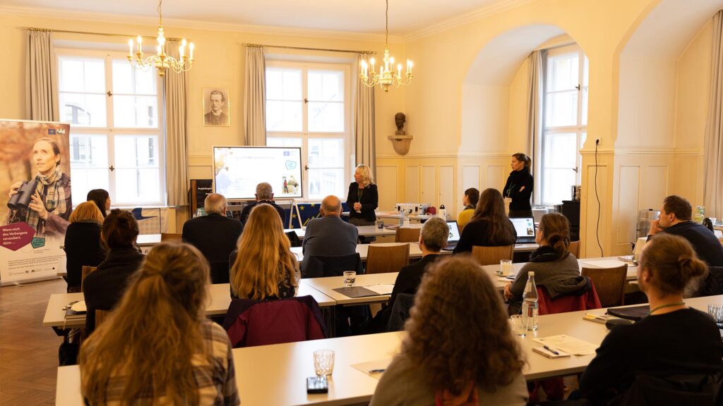 Die Mitglieder und Mitgliederinnen der Projektbegleitenden Arbeitsgruppe LIFE sitzen gemeinsam in einen Besprechungsgraum in München.
