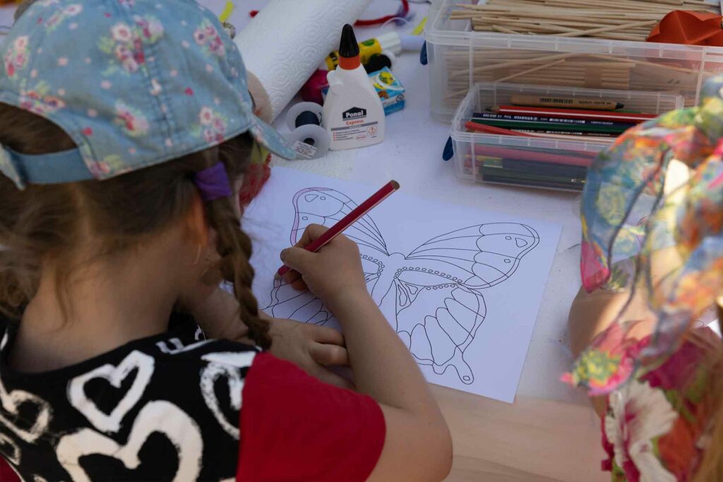Ein Kind malt eine Schmetterlingsvorlage aus.